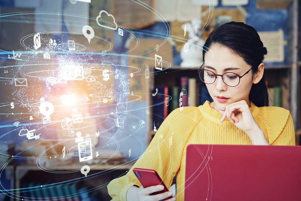 A young woman looking at cell phone in front of an open laptop.