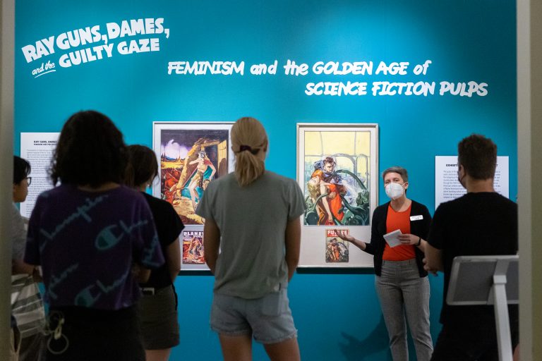 Amanda Douberley, assistant curator and academic liaison of the William Benton Museum of Art, shows students around the “Ray Guns, Dames, and the Guilty Gaze: Feminism and the Golden Age of Science Fiction Pulps” exhibition on display in the museum