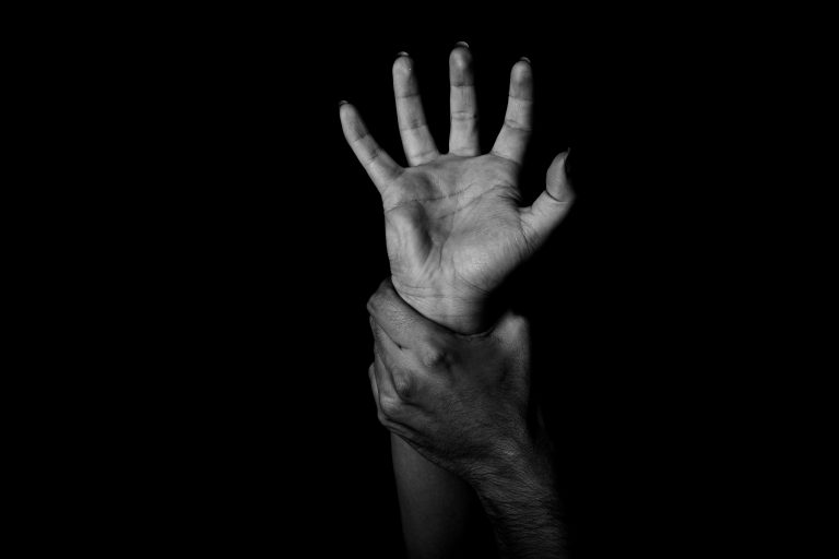 A Black person's hand, open, being grabbed at the wrist against a dark background.
