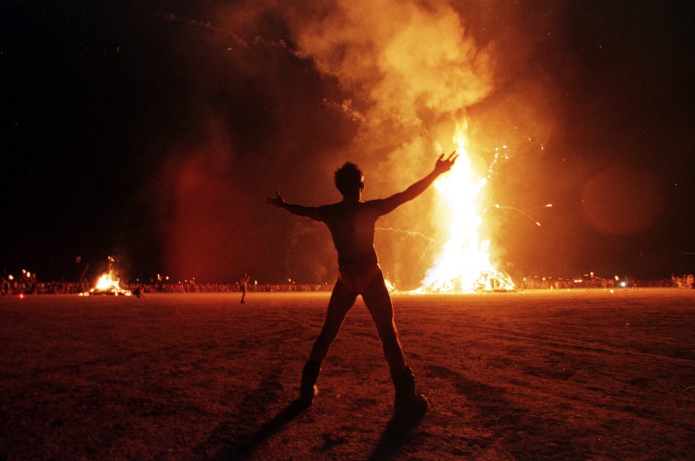 A "Burning Man" participant holds up his arms as t