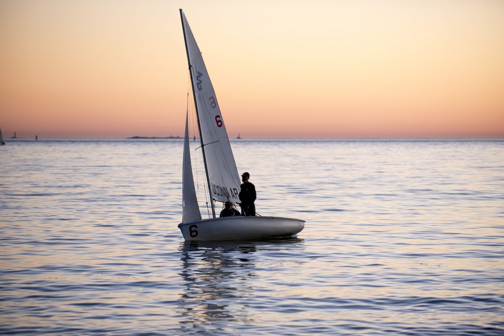 A sailboat on the water, with a setting sun on the horizon.