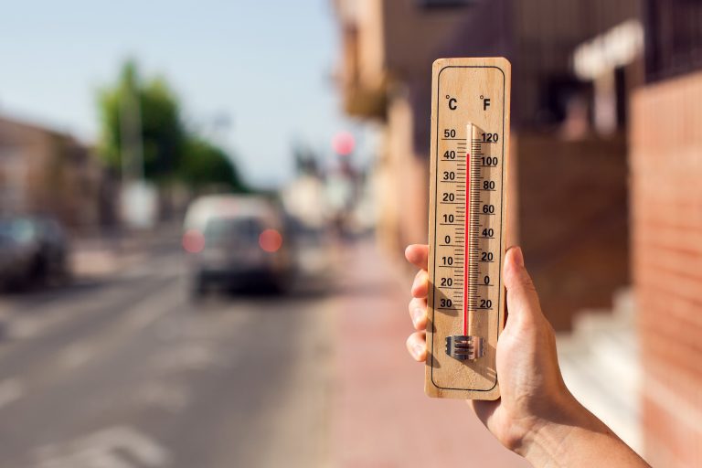 Hot weather. Thermometer in hand in front of an urban scene during heatwave.