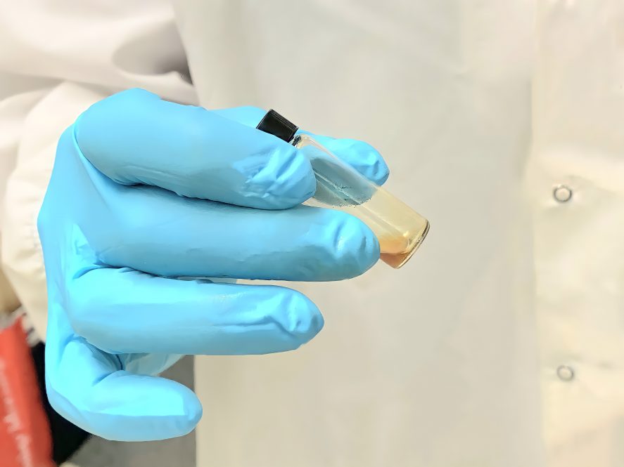 A researcher's gloved hand holds a vial of a brown liquid.