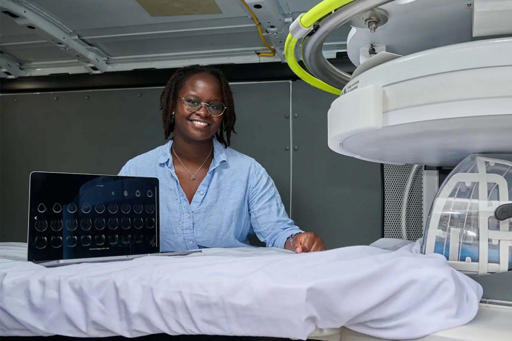 Amanda Yagan standing by an MRI machine with a laptop showing brain scans