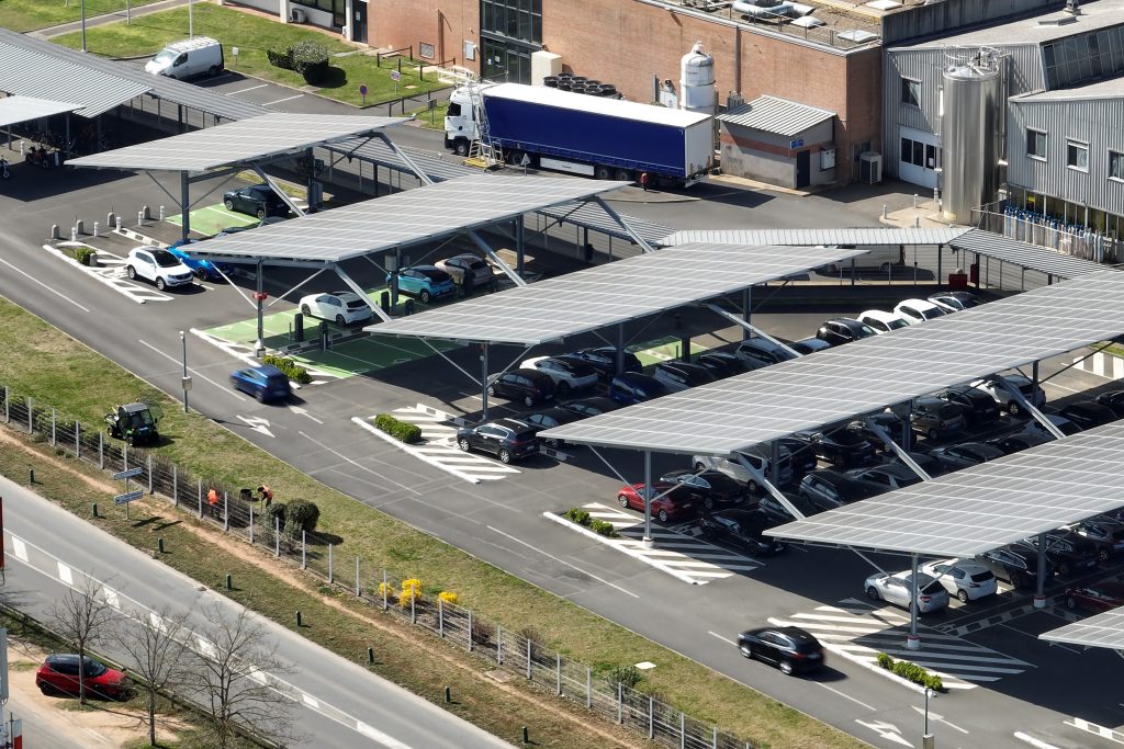 Aerial view of solar panels installed as shade roof over parking lot with parked cars for effective generation of clean electricity. Photovoltaic technology integrated in urban infrastructure.