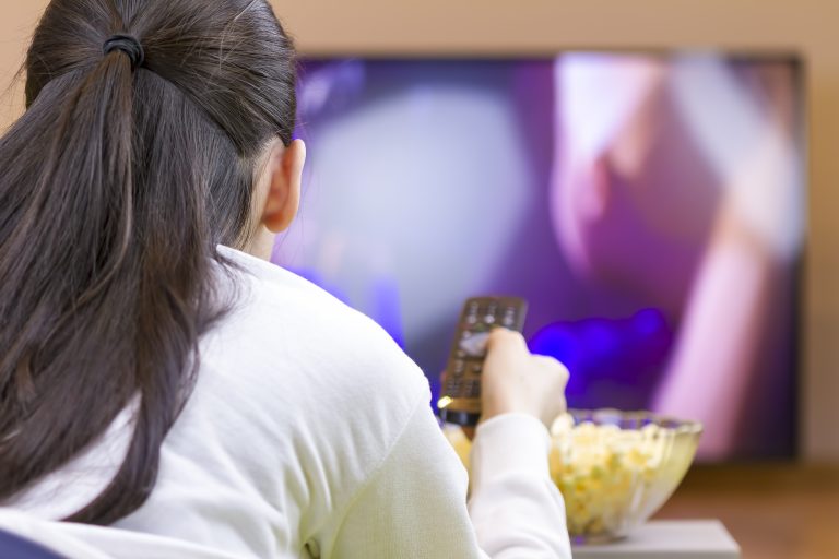 A young girl watches television with a bowl of unhealthy snacks in front of her.