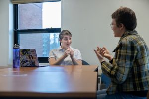 2022-23 American Sign Language (ASL) Community Housing Coordinator Lauren Gobler, left, and 2023-24 ASL Community Housing Coordinator Vivian London, right, have a conversation in ASL in one of the lounges of Watson Hall—the current home of UConn’s ASL Community Housing.