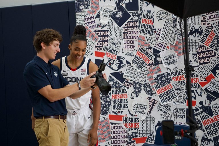 Jared Beltz '23 (SFA) shows photographs he took to UConn women's basketball junior forward Aubrey Griffin during a recent media day event he organized as an intern in a creative partnership between the Digital & Media Design and Athletics departments.