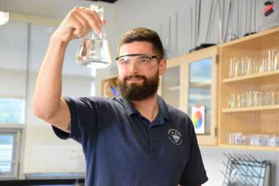 Mike Fenn in a science classroom holding a beaker.