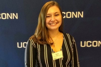 Jenna Racca smiles in front of a UConn banner.