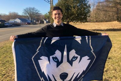 Rowan Page smiles and holds up UConn Husky banner.