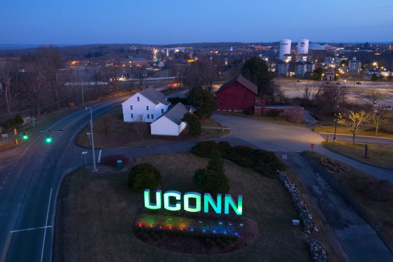 Drone views of the UConn entryway sign lit in green light.