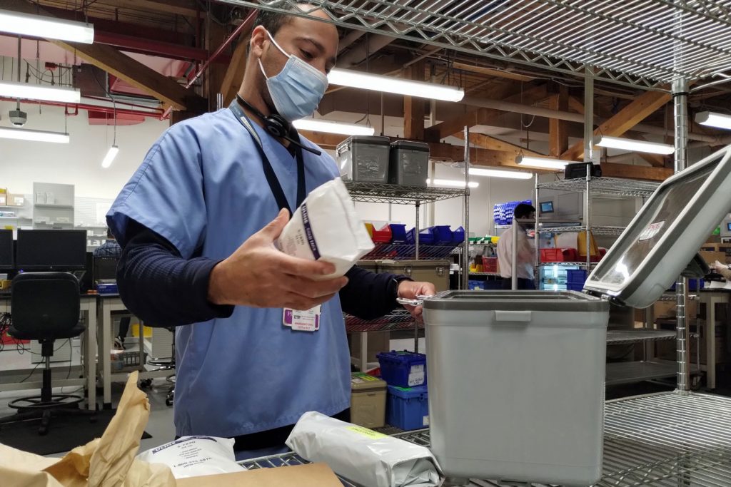 Pharmacy technician loads resuable medication transport container