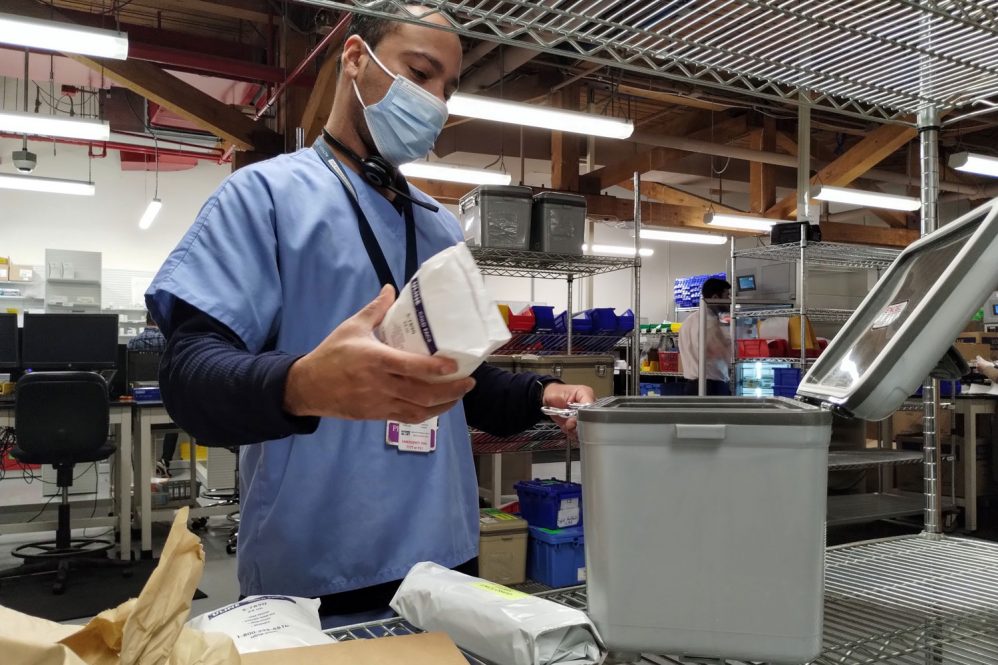 Pharmacy technician loads resuable medication transport container