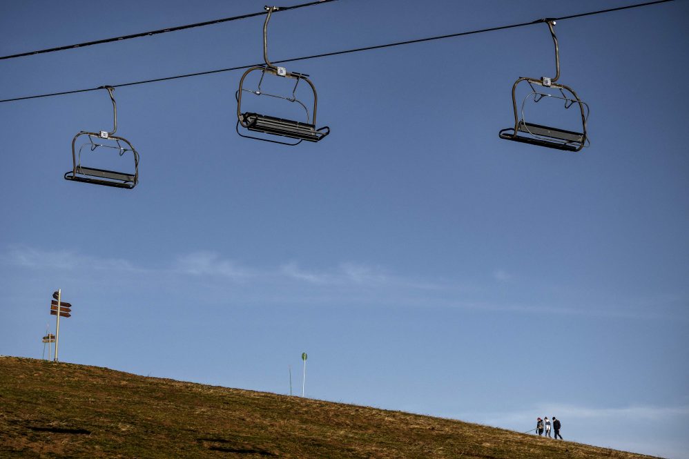 Ski lifts drift over a green field as people walk in the distance.
