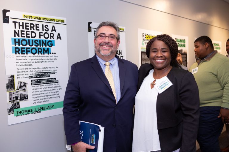 Fernando Betancourt and Fiona Vernal smile in front of exhibit posters.