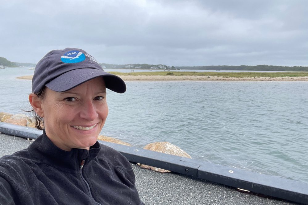 Lisa Milke, a shellfish research expert, has been appointed as the new head of NOAA’s ecosystems and aquaculture division and is pictured standing by a body of water in a NOAA hat