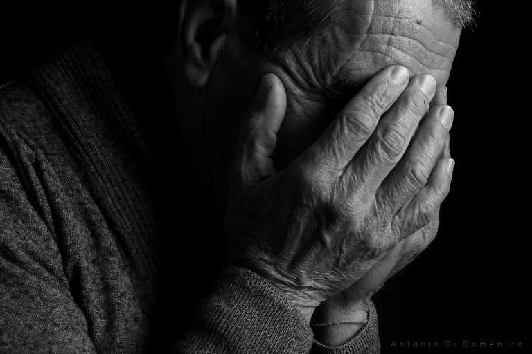 An older man covers his face with his hands in a sign of severe depression.