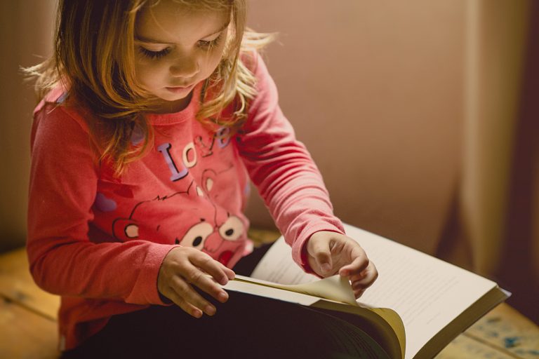 A young girl in a pink sweatshirt reads a book.