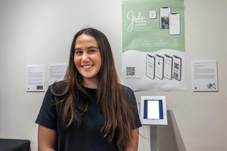 Senior digital media design student Giana Adragna poses for a photo in front of her project on display in the digital media and design program's 
