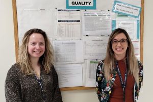 female lab employees in front of a quality metrics display