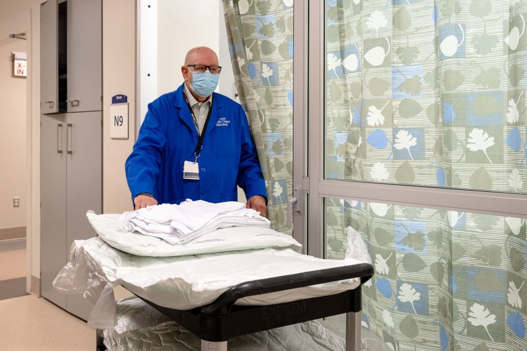 Volunteer in blue coat pushing cart of linens in emergency department