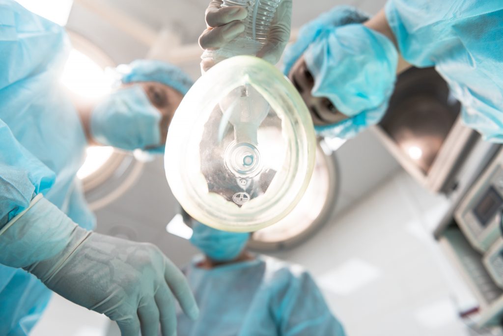 Bottom view of three professional doctors leaning over the patient and wearing medical masks while holding the anesthetic inhaler.