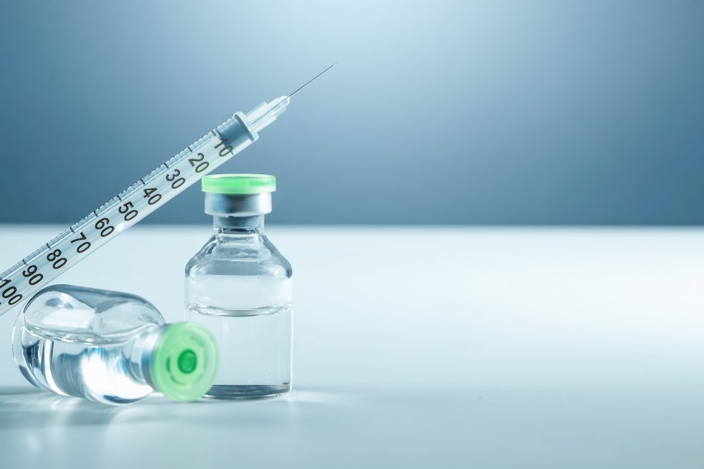 Vaccine in vial and syringe close-up on a white table gray background.