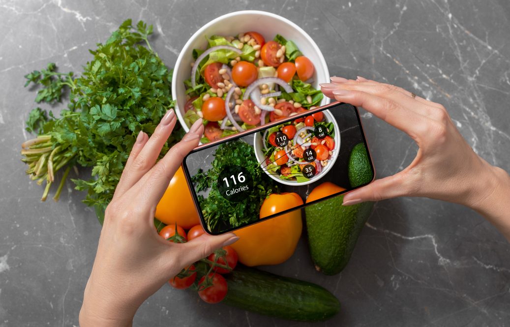A woman holds her smartphone above a salad bowl, tracking the calories of the food on a dieting app.