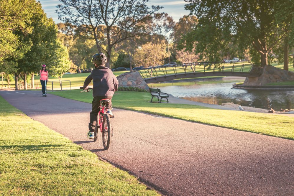 Boy riding his bicycle along the bike lane in an urban park.