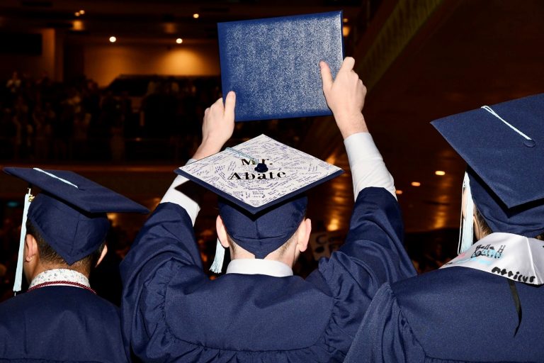 A graduate holds their diploma cover above their head