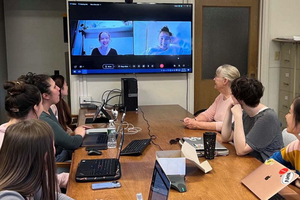 UConn professor Sara Harkness, top right, and her class of students in Spring 2023. On the monitor, two students from Radboud University in the Netherlands join class remotely as part of a virtual study exchange.