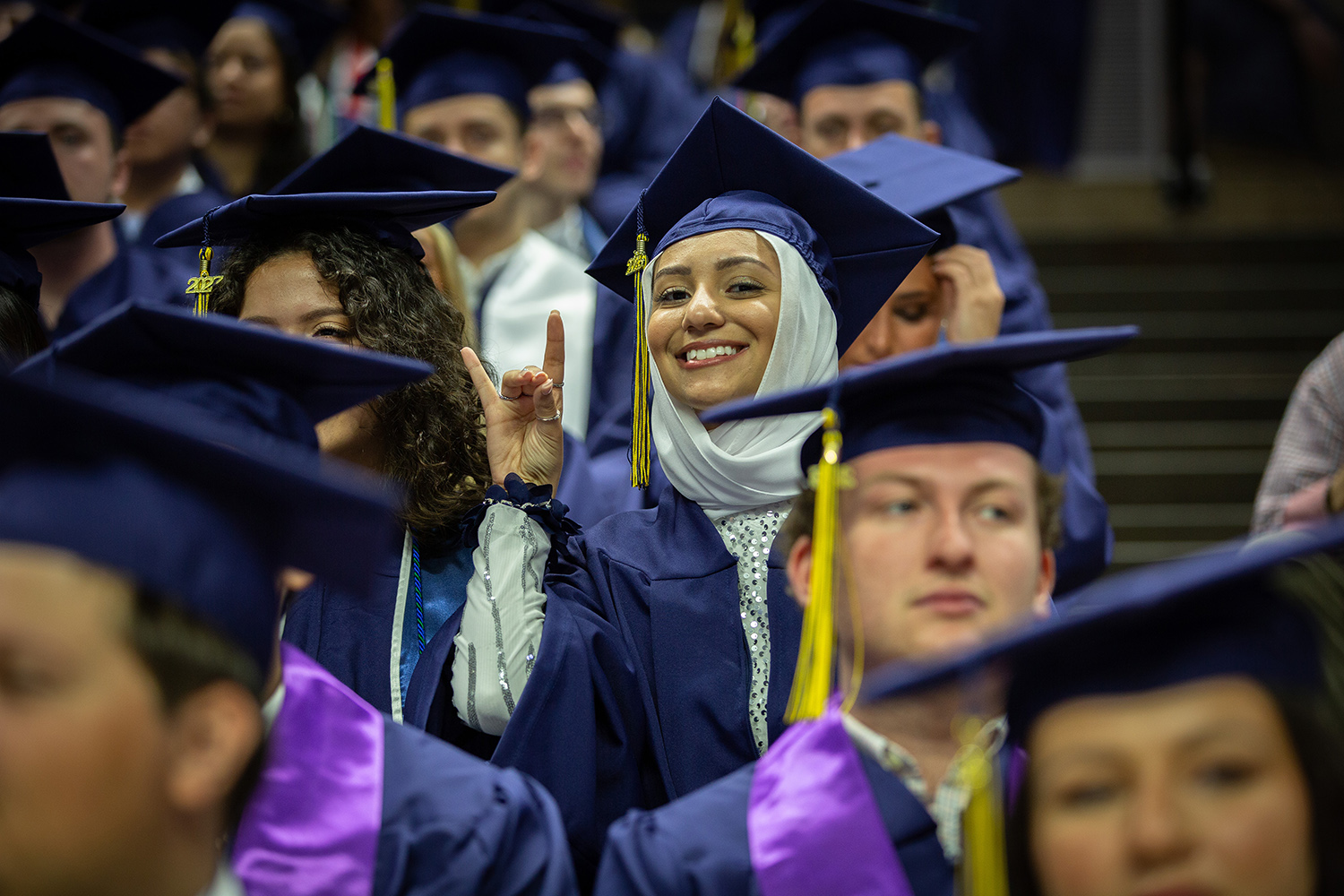 A graduate smiles for photo while making the husky sign with hand.