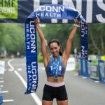 runner with medal holds finish line above her head