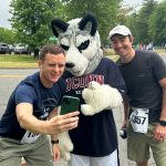 two men taking selfie with Husky mascot