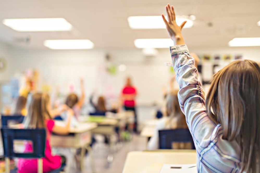 A young girl raises her hand in an elementary school classroom.