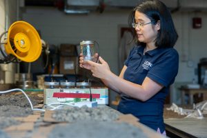 Huijie Gan, an assistant research professor in the Department of Plant Science and Landscape Architecture, holds a soil sample she used for a project to assess soil health amidst a collection of other soil samples
