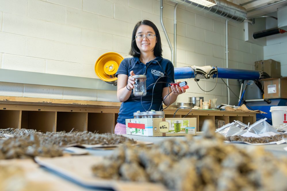 Huijie Gan, an assistant research professor in the Department of Plant Science and Landscape Architecture, holds a soil sample and sensor she used for a project to assess soil health amidst a collection of other soil samples