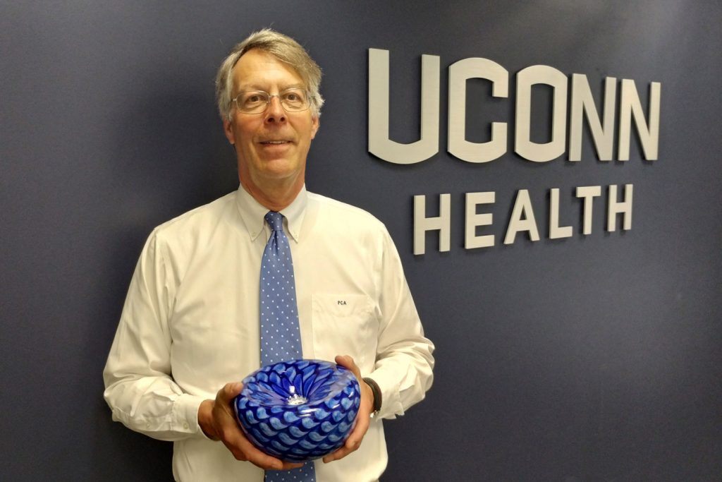 Dr. Albertsen holding glass bowl in front of UConn Health sign