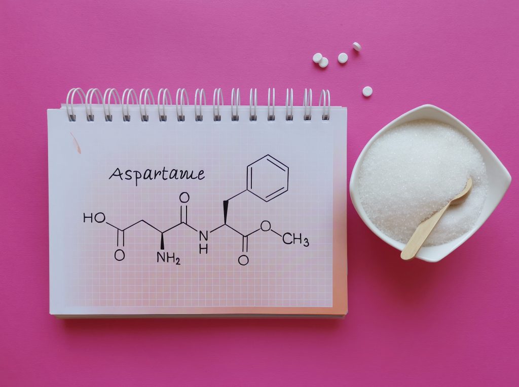 A notepad showing the chemical diagram of the artificial sweetener aspartame next to a bowl of it.