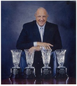 Former UConn Athletics Director Lew Perkins poses with four championship trophies.