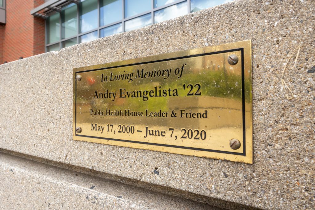 A plaque commemorating the Andry Evangelista Memorial Garden hangs with a reflection of part of the garden outside the Peter J. Werth Residence Tower.
