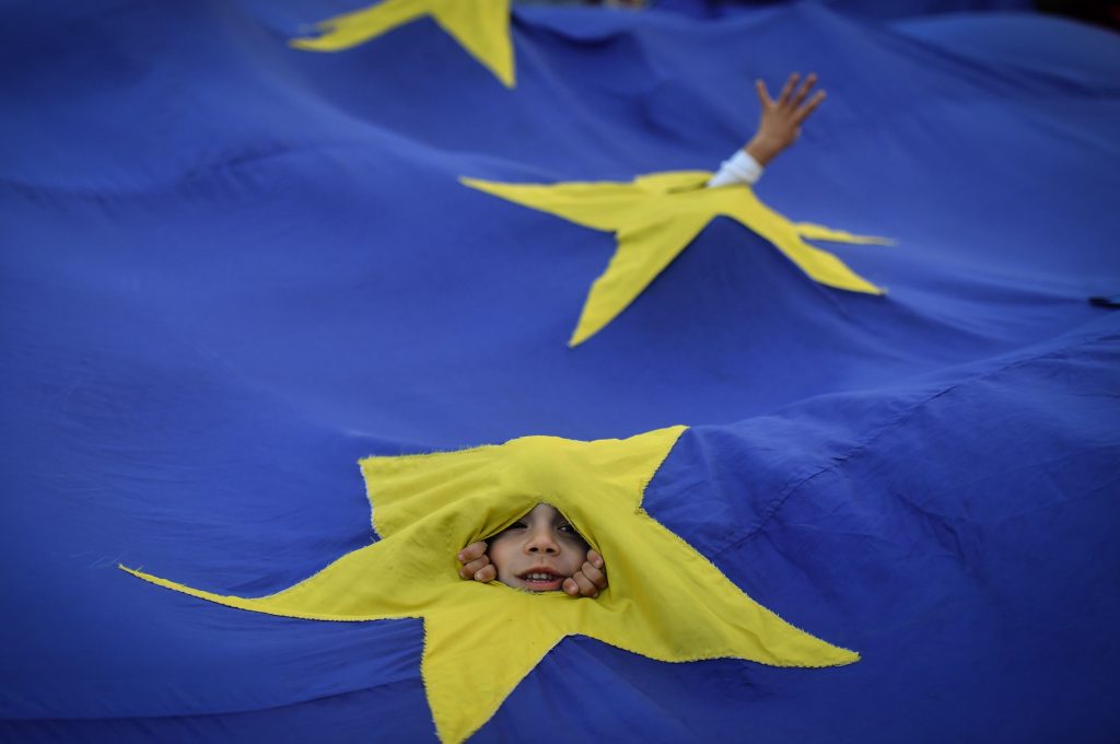 A child peeks through a hole in a huge European Union flag during a demonstration.