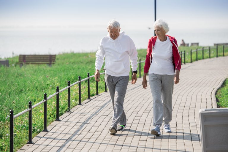An active senior couple walks along a stone path on a sunny day while chatting.