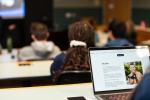A student looks at the personal website of speaker Neil Mandt while he gives a lecture to a class.