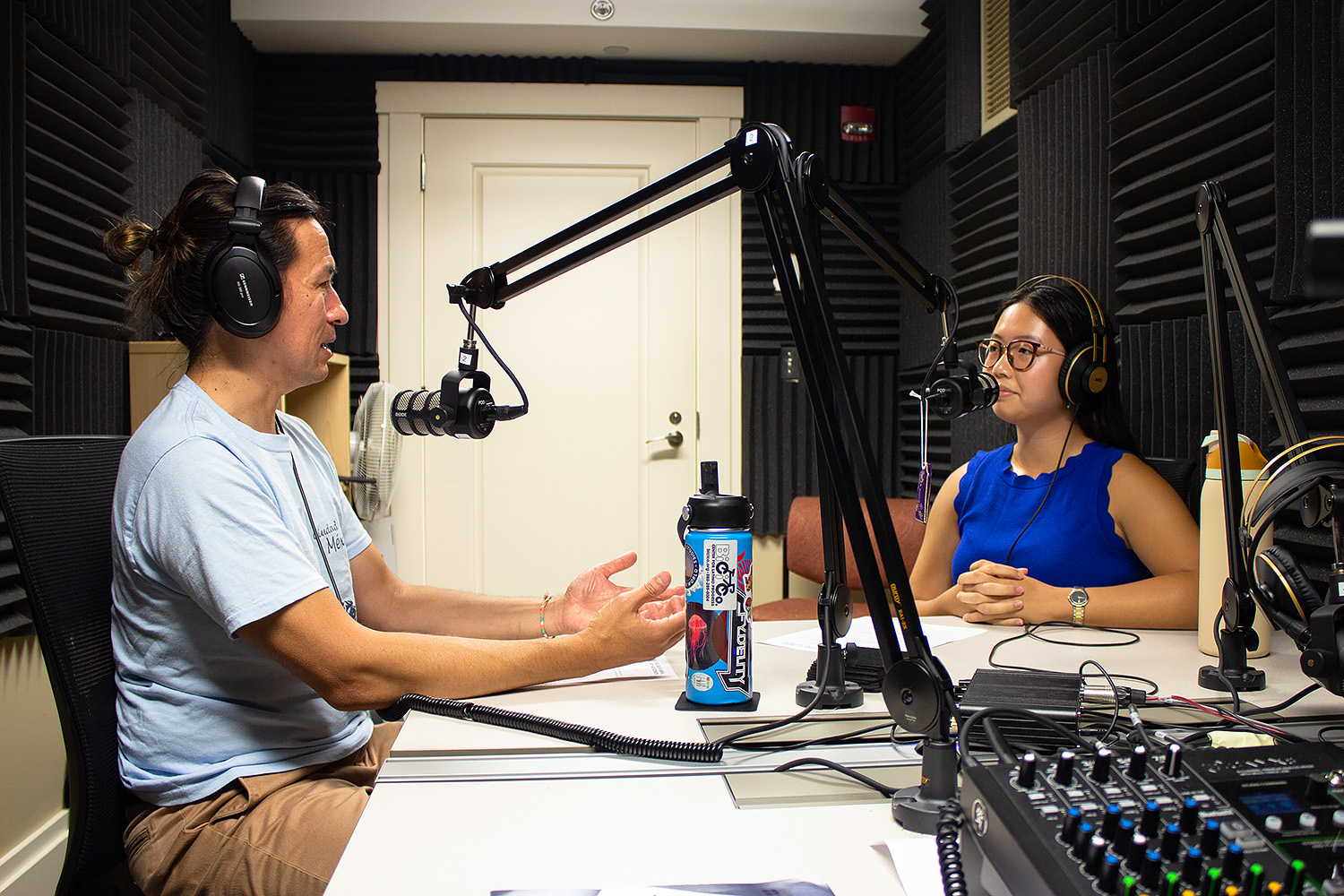 Jason Chang and Karen Lau sit in front of microphones in a recording studio.