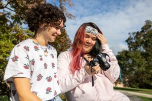 Remi Dupuis '26, left, and Alexa Udell '24 look through photos of Dupuis that Udell took for her photography project that highlights transgender students at UConn in the shade garden near the Benton Museum
