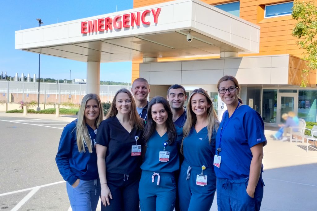 Group portrait of physician assistants in scrubs outside emergency department entrance
