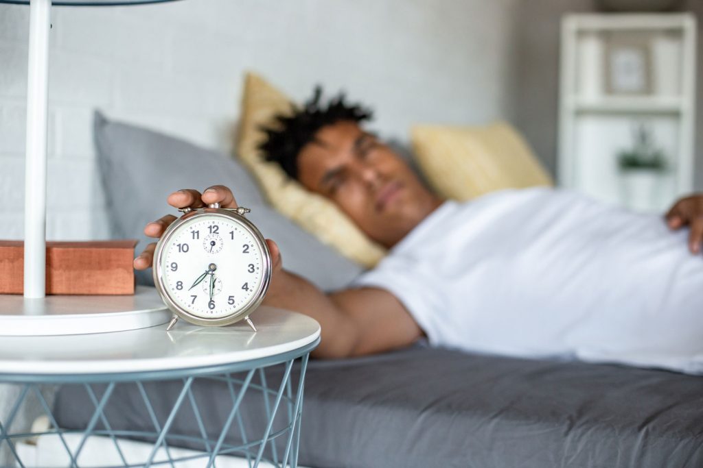 young African American man waking up and turning the alarm off