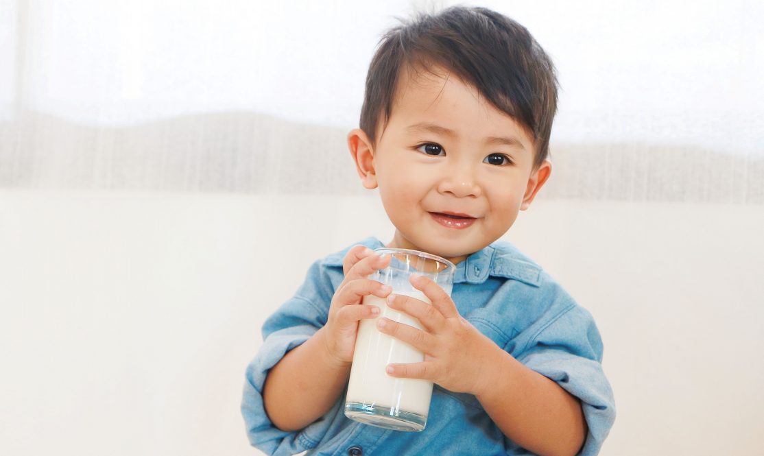 A young child holds a glass of milk.